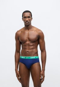 Σκούρα μπλε εσώρουχα Nike με πράσινη ελαστική ζώνη μέσης που φέρει το λογότυπο της Nike. Λείο ύφασμα με εφαρμοστή σχεδίαση, μινιμαλιστικό σχήμα.