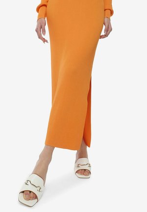 Orange ribbed midi dress with a side slit, paired with white slide sandals featuring a gold chain accent.