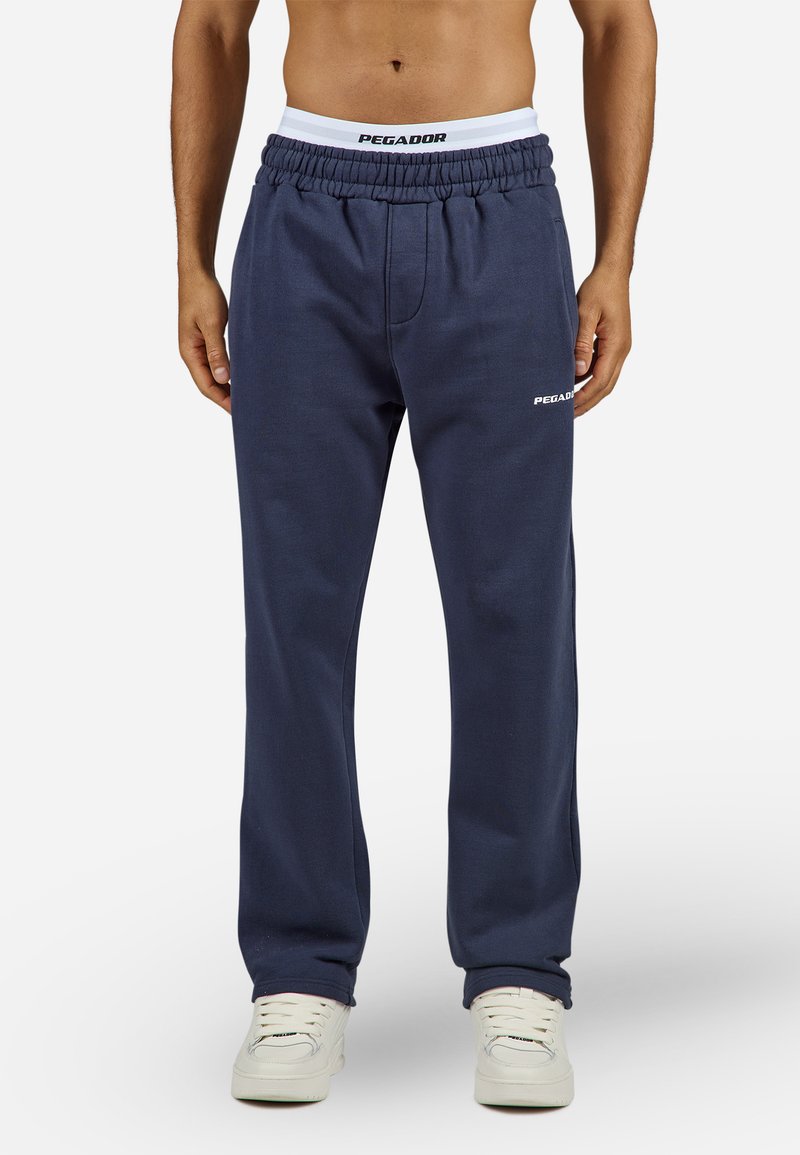 Navy sweatpants made of cotton blend, featuring a drawstring waist, side pockets, and "PEGADOR" logo in white on the left thigh.
