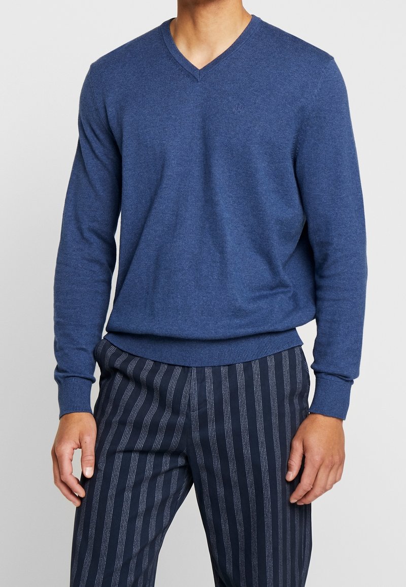 Blå V-ringad tröja i mjukt tyg, med långa ärmar och åtsmitande midja. Tillsammans med marinblå byxor med ränder.