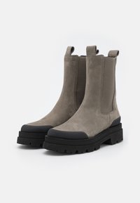 Paar graue Wildleder Chelsea-Boots mit schwarzen, stabilen Gummisohlen und verstärkten Zehenkappen, ausgestattet mit Zuglaschen und elastischen Seitenpaneelen.