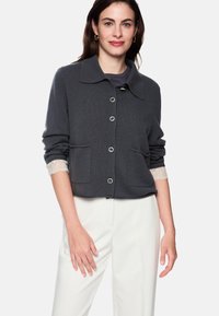 Dunkelgrauer Cardigan mit klassischem Kragen, Knopfleiste, zwei vorderen Taschen und Spitzenakzenten an den Ärmelbündchen. Weiche Textur, kurz geschnittenes Design.