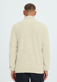 Cremfarbene Fleece-Jacke mit einer weichen, strukturierten Oberfläche, langen Ärmeln und einem hohen Kragen. Hat einen geraden Saum und keine sichtbaren Beschläge.