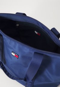 Bolso tote de nailon en color marino con cierre de cremallera, que presenta un pequeño parche con el logotipo y un forro interior de contraste. Mangas duraderas para un fácil transporte.