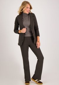 Donkergrijze blazer over een lichtgrijze turtleneck, gecombineerd met donkere broek en bruine sneakers met witte strepen. Eenvoudig, op maat gemaakt ontwerp.