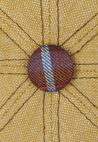 Textured yellow fabric with woven pattern, featuring a central button in orange, blue, and red stripes. Detailed stitching radiates from the button.