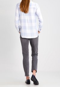 Lys blå og hvid ternet skjorte, lange ærmer, knapmanchetter, parret med mørke grå slim-fit jeans og sorte sko.