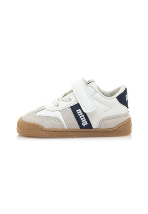 Zapatilla deportiva blanca con acentos de ante gris, franja azul marino y correa de Velcro. Presenta una suela de goma con agarre texturizado para mayor durabilidad.