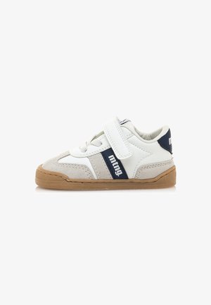 Zapatilla deportiva blanca con acentos de ante gris, franja azul marino y correa de Velcro. Presenta una suela de goma con agarre texturizado para mayor durabilidad.