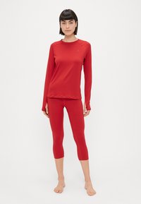 Conjunto atlético vermelho que inclui uma blusa de manga longa e leggings curtas, feito de um tecido liso e elástico com costuras mínimas e um logotipo discreto.