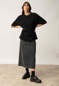 Černý oversized pletený svetr s širokými rukávy, kombinovaný s celkově vysokým šedým denimovým sukní střední délky a černými platformovými botami.
