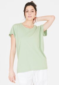 Ljusgrön kortärmad t-shirt i mjuk bomull. Rund halsringning, avslappnad passform och upprullade ärmar, tillsammans med vita byxor.