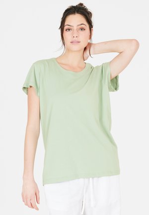 Lysegrøn kortærmet t-shirt lavet af blødt bomuld. Rund halsudskæring, afslappet pasform og foldede ærmer, parret med hvide bukser.