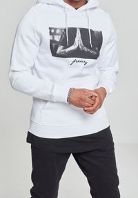 Witte hoodie met een voorkantafbeelding van biddende handen en het woord "pray". Voorzien van trekkoorden, een kangoeroezak en geribbelde manchetten.