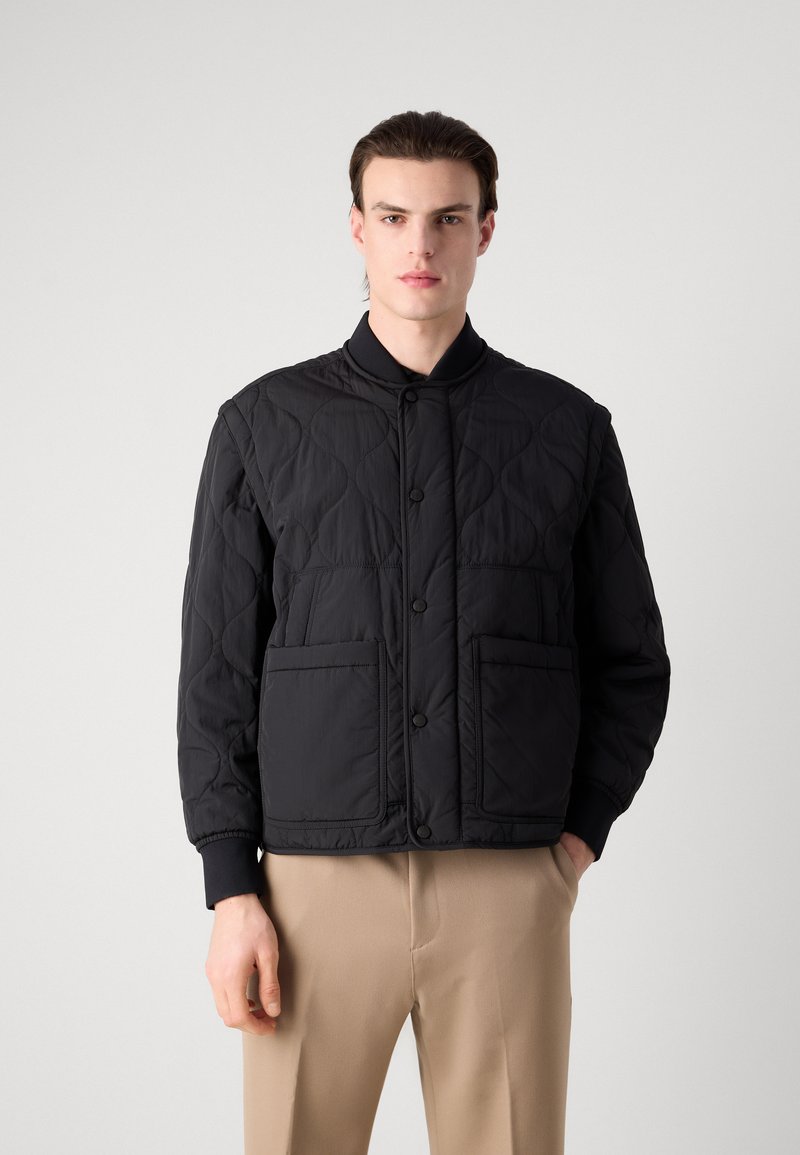 Schwarze gesteppte Jacke mit Stehkragen, ausgestattet mit zwei großen Fronttaschen, Knopfverschluss und gerippten Bündchen. Hergestellt aus leichtem Material.