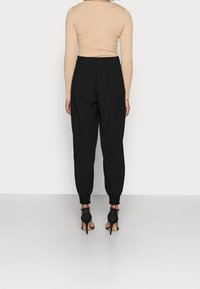 Svarta tapered joggers med elastisk midja, tillsammans med en ribbad långärmad beige topp och svarta högklackade skor.