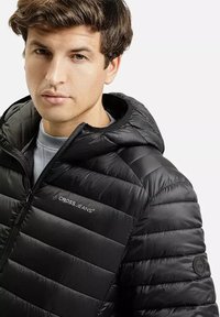 Czarna kurtka pikowana z kapturem, z poziomym przeszyciem, zamek błyskawiczny z przodu i małym logo na piersi. Gładka, błyszcząca tekstura.