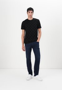T-shirt noir à manches courtes avec un motif texturé, associé à un jean noir délavé et des baskets blanches. Conception simple et ajustée.