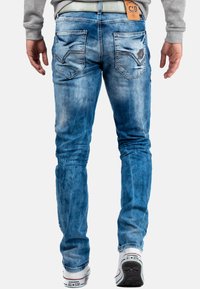 Jean en denim bleu avec une texture décolorée, cinq poches et des coutures distinctes sur les poches arrière. Portés avec des baskets blanches.