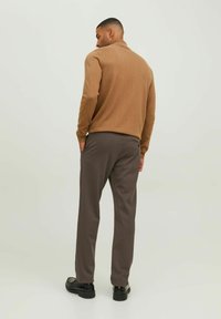 Suéter de punto marrón con cuello alto, combinado con pantalones tapered gris oscuro y zapatos negros, visto desde la espalda.