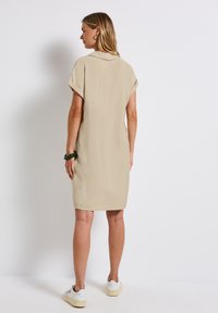 Beige kortärmad klänning med krage, texturerat tyg, knä-lång längd och bärs med vita sneakers.