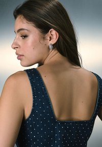 Denimkleit laiade rihmade ja sügava seljaga, kaunistatud hõbedaste helmedega. Kanda tekstuursete hõbedaste kõrvarõngastega, mis näitavad sujuvat tumedat viimistlust.