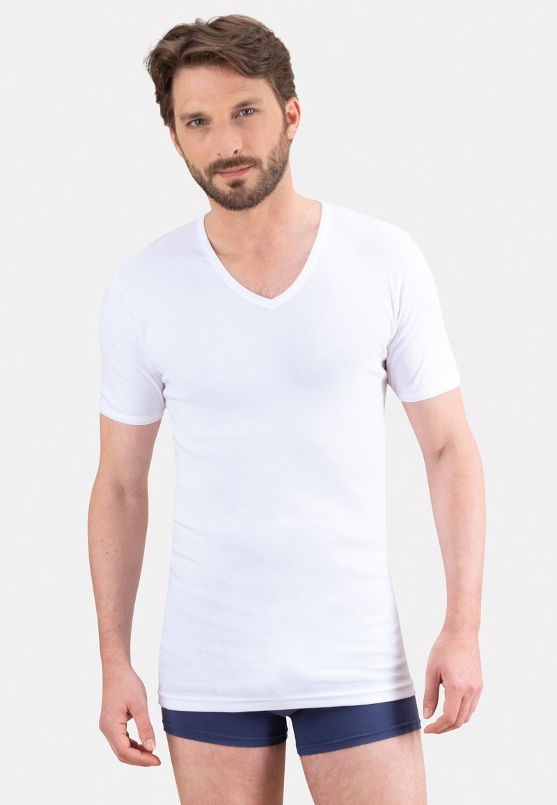 T-shirt blanc à manches courtes et col en V, fabriqué en tissu doux, avec une coupe ajustée et un col simple. Porté par-dessus un short de boxeur bleu foncé.