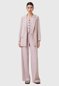 Completo pantalone rosa chiaro con giacca lunga, gilet con bottoni e pantaloni a gamba larga in un tessuto morbido. Nessun motivo o accessorio visibile.