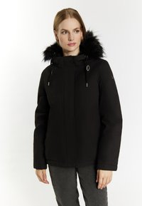Sort polstret jakke med faux fur hætte, justerbar snøre, lynlås foran og elastiske manchetter. Har en glat tekstur og et ensartet design.