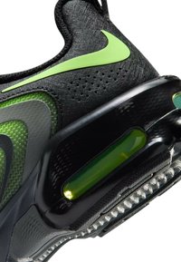 Talons de chaussure de sport Nike noirs et verts avec semelle à coussin d’air et logo Nike swoosh vert vif sur matière supérieure texturée.