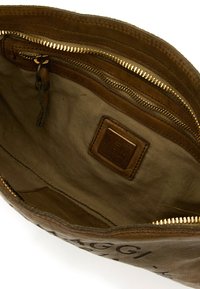 Interno di borsa in pelle marrone con rivestimento in tessuto beige, cerniera dorata e etichetta del marchio in pelle cucita all'interno della borsa.