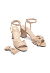 Beżowe sandały na wysokim obcasie z odkrytymi palcami, pasek na kostkę i akcent w postaci kokardki na palcach. Zawiera pasującą klamrę w kształcie kokardki.