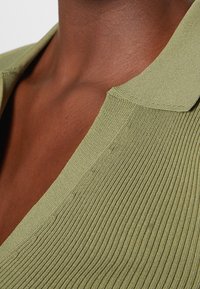 Oliwkowa, prążkowana koszulka polo z kołnierzykiem, teksturowana tkanina oraz dopasowany krój. W zbliżeniu widać kontury wokół szyi.