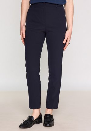 Pantalons tailleur marine à coupe slim et texture lisse, dotés de passants de ceinture et d'une fermeture éclair. Associés à des mocassins noirs pour un look formel.