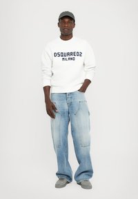 Valge sweatshirt tumesinise "DSQUARED2 MILANO" tekstiga, helesinised laiad teksad, hall müts ja hallad spordijalanõud.
