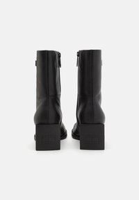 Black leather ankle boots with a block heel, featuring a side zipper and a textured logo accent on the heel. Smooth finish, sleek design.