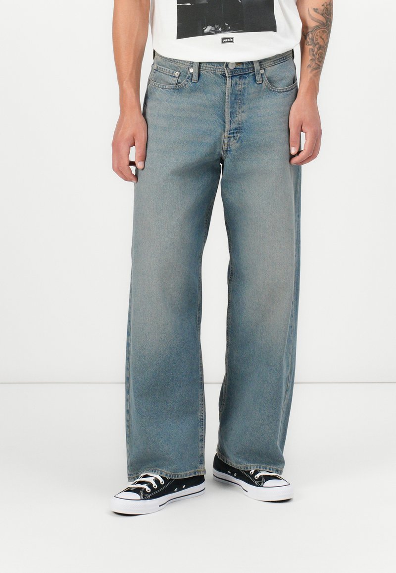 Lyseblå denim bukser med vid ben som har en falmet finish, fem lommer og bæltesløjfer, parret med sort og hvide lavt top sneakers.