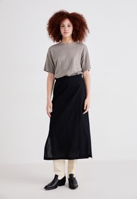 Grijze top met korte mouwen, gecombineerd met een lange zwarte rok, gedragen over crèmekleurige broeken. Zwarte hoge laarzen maken de outfit compleet.