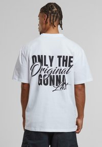 White cotton t-shirt with short sleeves, featuring large black text on the back: "ONLY THE Original GUNNA Last." Standard fit.