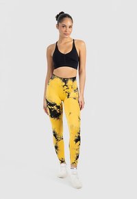 Czarny krótki top na ramiączkach z marszczonym przodem, zestawiony z żółto-czarnymi legginsami tie-dye. Legginsy mają wysoki stan i elastyczny materiał.