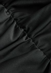 Gros plan d'un tissu noir avec des coutures rassemblées créant un motif froncé texturé et un tissage côtelé fin visible.