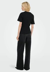 Sort T-shirt med korte ærmer, rund halsudskæring og tætsiddende design, parret med sorte bukser med bred ben. Begge beklædningsgenstande har glatte teksturer.