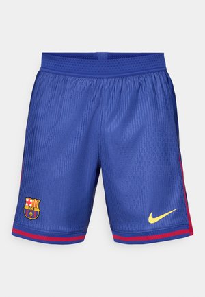 Blue football shorts with mesh fabric, featuring a striped red side accent, Barcelona logo, and yellow Nike swoosh.