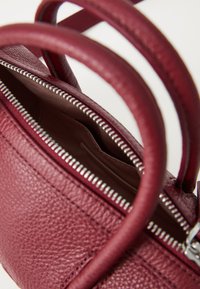 Leather handbag in deep burgundy with a textured finish. Features zip closure, short handles, and interior slip pocket.