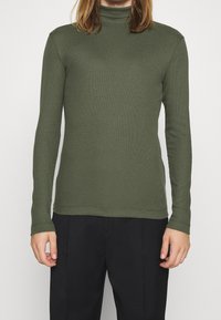 Oliven grøn turtleneck skjorte lavet af ribbet stof, med lange ærmer og en tætsiddende design. Glat tekstur med en sømløs finish.