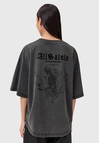 T-shirt overdimensionato grigio scuro, in materiale cotone, con una grafica nera sul retro che presenta elementi floreali e scheletrici.