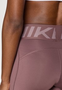 Κολάν υψηλής μέσης σε ανοιχτό μωβ χρώμα με ανάγλυφη υφή υφάσματος, ραφές flatlock και έντονο, τονι κό λογότυπο Nike στη μέση.