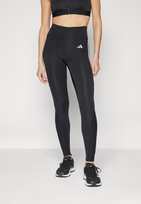 Leggings sportivi neri con vita alta, dotati di strisce bianche lungo i lati e di un piccolo logo bianco sulla coscia sinistra. Tessuto morbido.