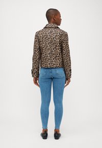 Jakna s leopard uzorkom, s otvorenom reverzom, prilagođenim krojem i dugim rukavima, u kombinaciji s plavim uskim trapericama i crnim cipelama.