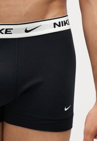 Gros plan d'une personne portant un boxer Nike noir avec une ceinture blanche arborant le logo Nike et des symboles swoosh.